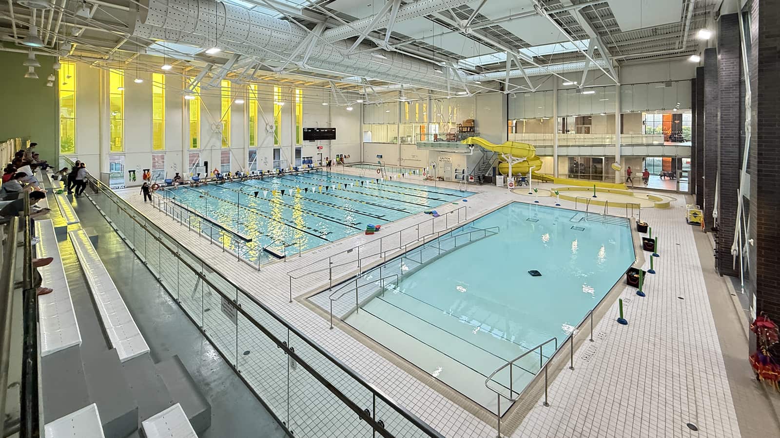 Piscina cubierta con carriles marcados y un tobogán amarillo al fondo