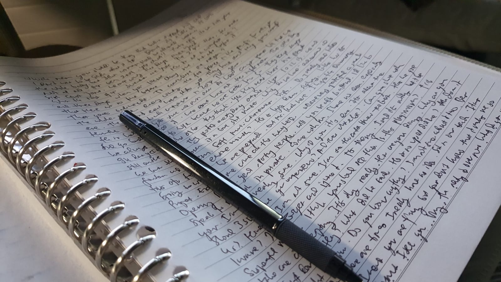 Cuaderno de espiral con una página llena de escritura a mano y un lapicero encima